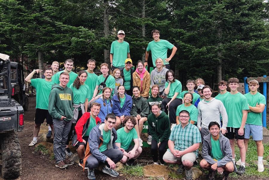 A group of students, wearing green t-shirts, smile and stand together.