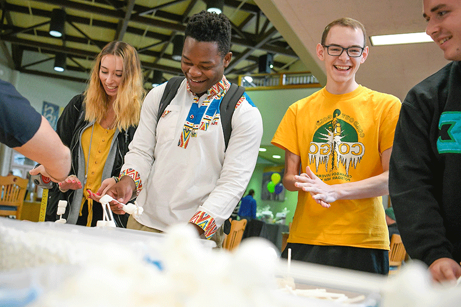 Students stand at a table and make houses out of sticks and marshmallows as part of a Clarkson Ignite event in the Educational Resources Center.